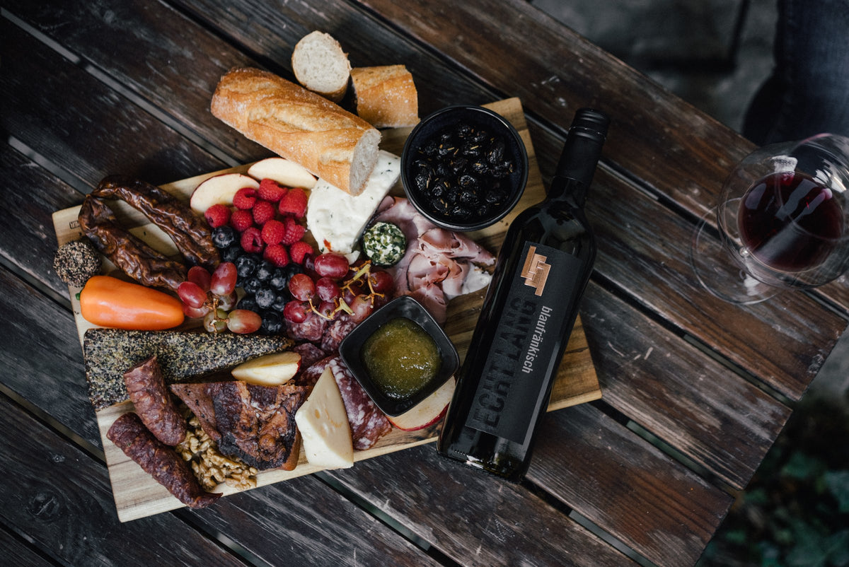 Jausenbrett mit Wurst, Käse und Beeren neben einer Flasche Blaufränkisch Echt Lang