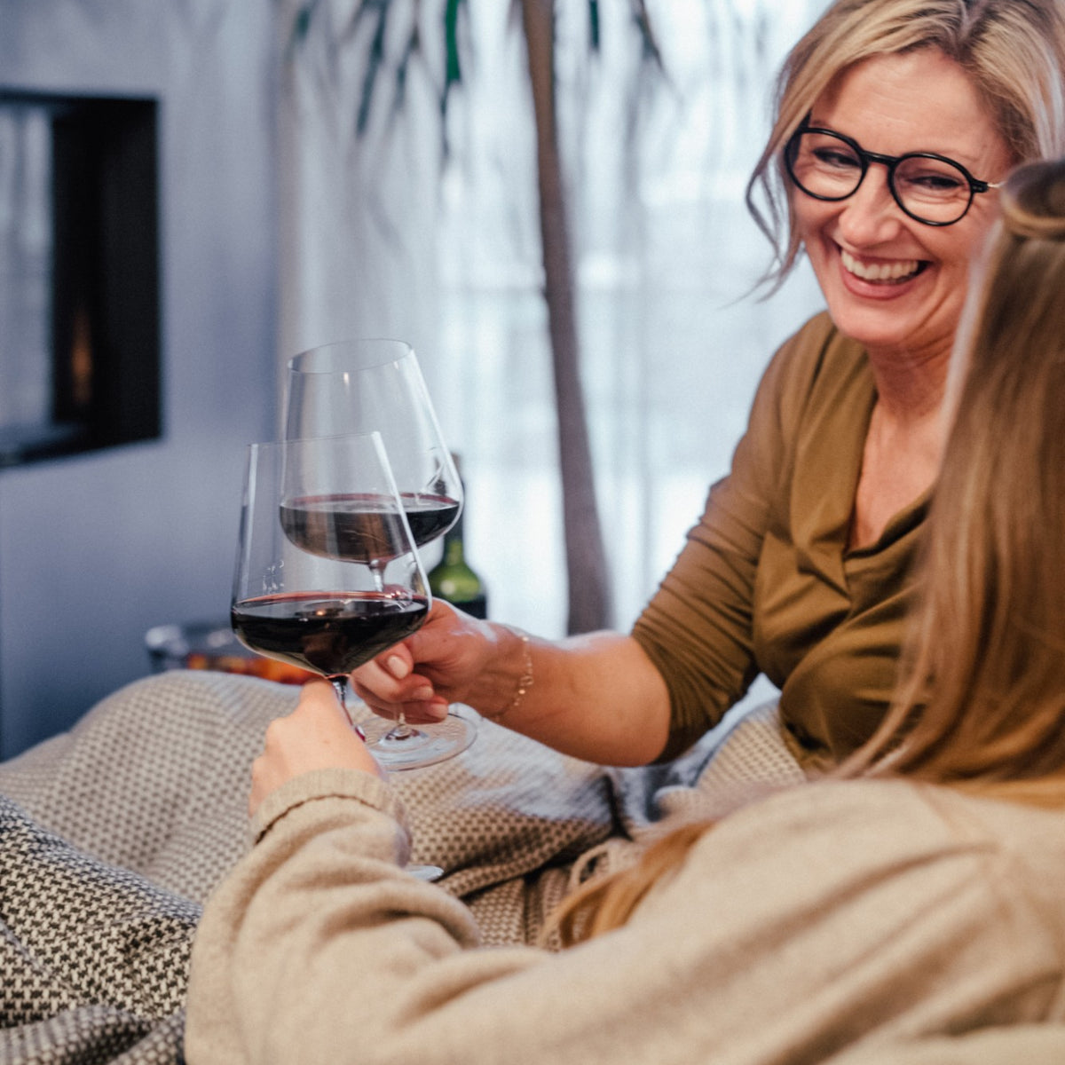 Zwei Frauen stoßen am Kamin lachend mit Rotwein an