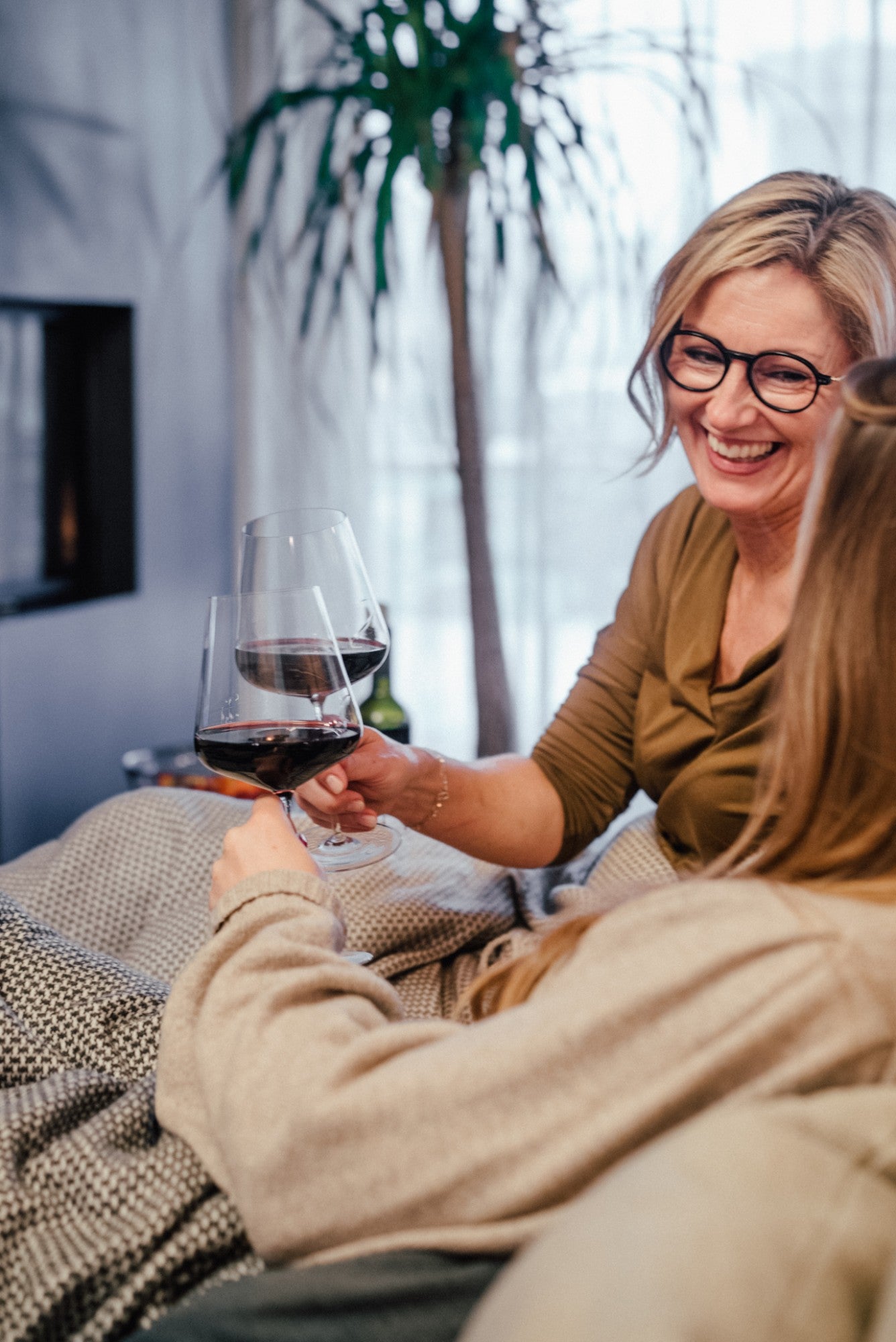 Zwei Frauen stoßen am Kamin lachend mit Rotwein an