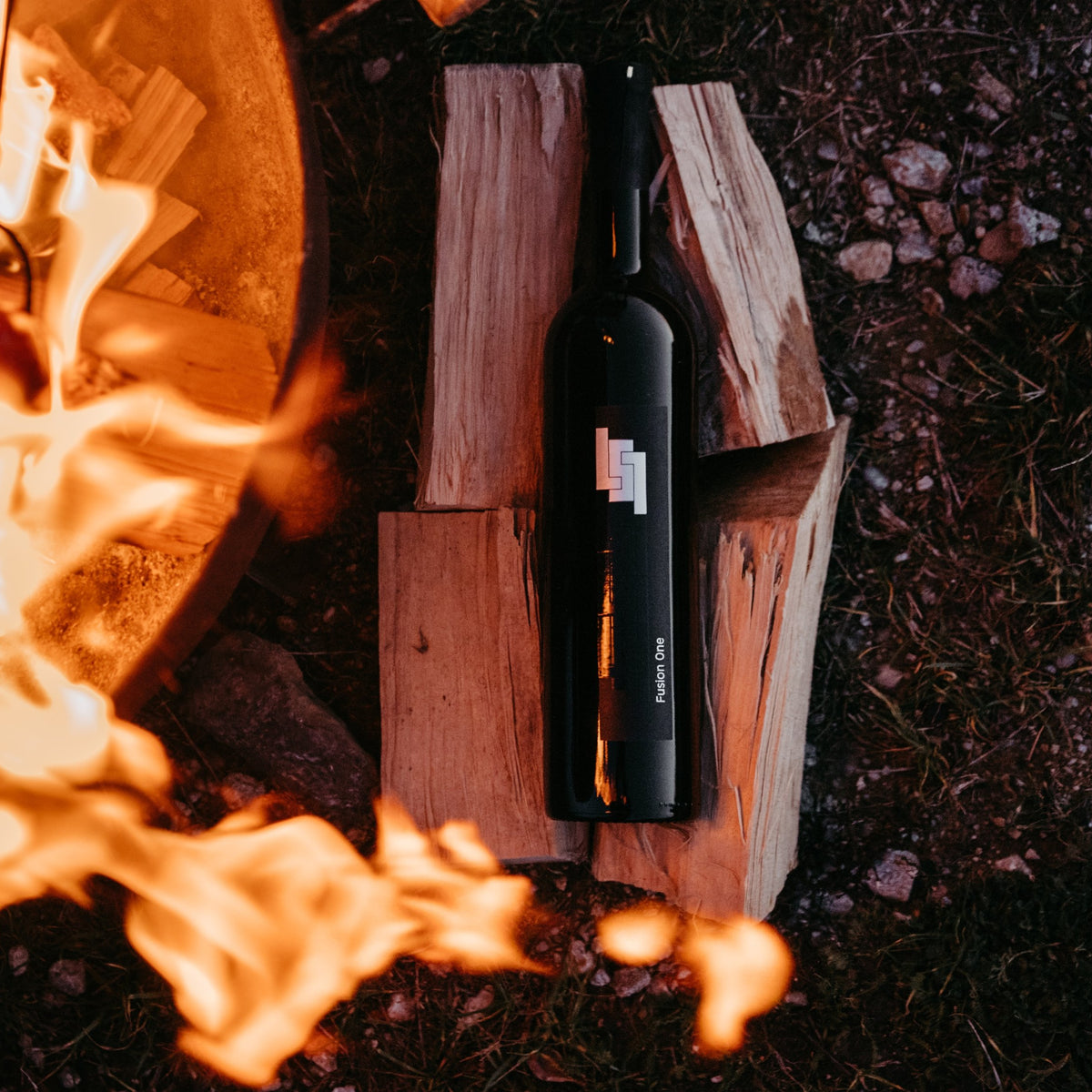 Flasche Cuvée Fusion One am Lagerfeuer, im Feuerschein liegend