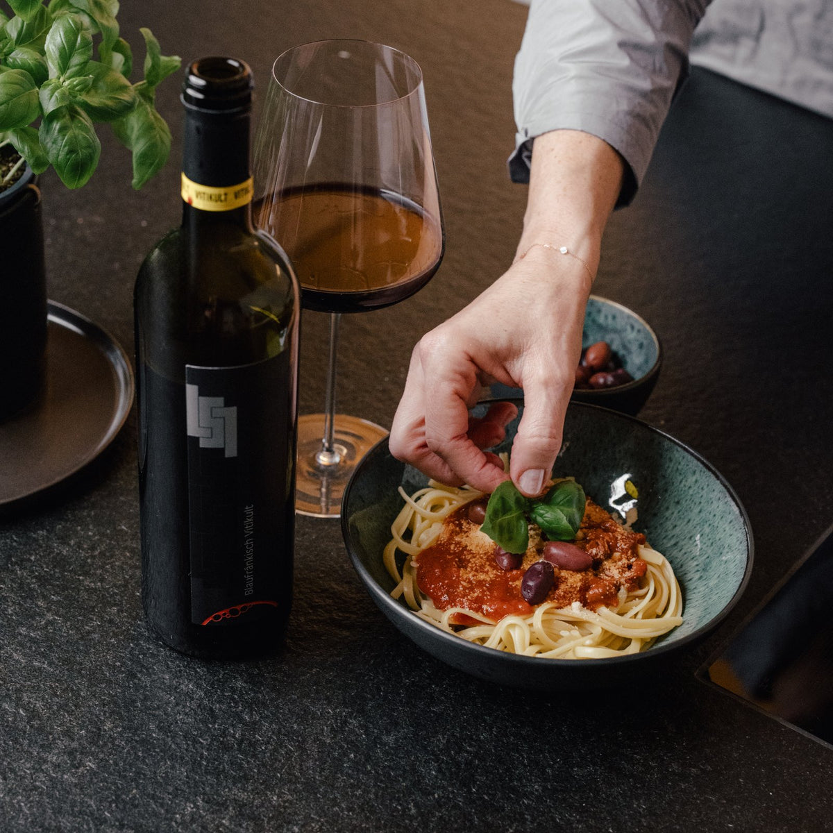 Teller Pasta mit einem Glas Rotwein und Flasche am Küchentisch